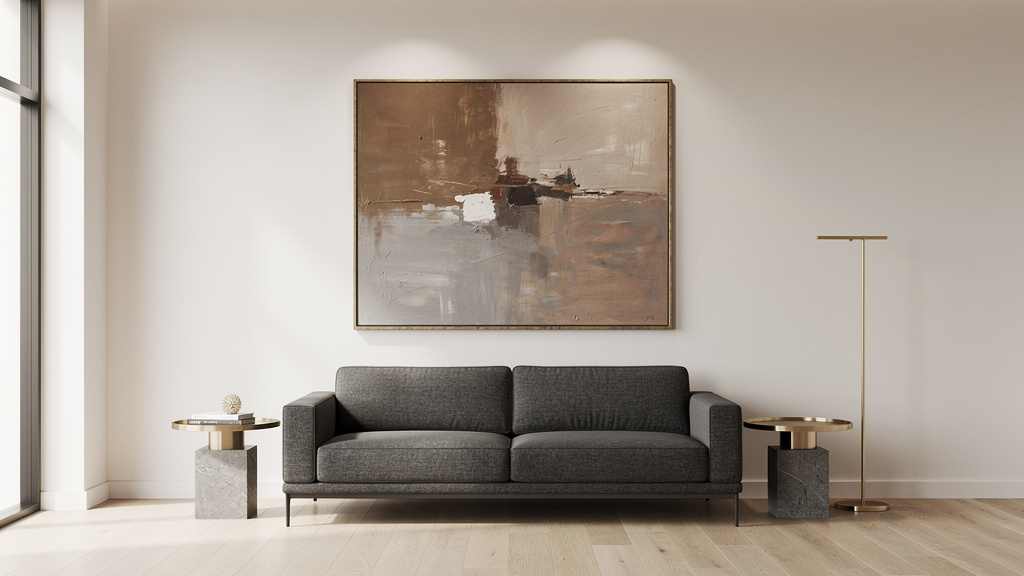 A large abstract painting in muted earth tones hangs on an off-white wall above a low graphite sofa in a sunlit, minimal